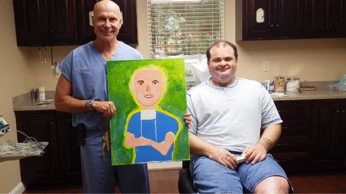 Dr Niamtu holding a portrait with his patient, Casey, who painted it